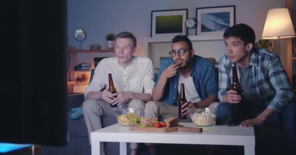 Fanáticos de los deportes viendo el juego en la televisión tintineo botellas riendo celebrando la victoria — Vídeos de Stock