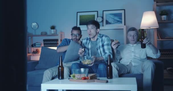 Парни смотрят страшные фильмы по телевизору и едят закуски, пьют пиво. — стоковое видео