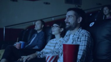 Sinemada film izleyen neşeli genç erkek ve kadınlar gülümseyerek