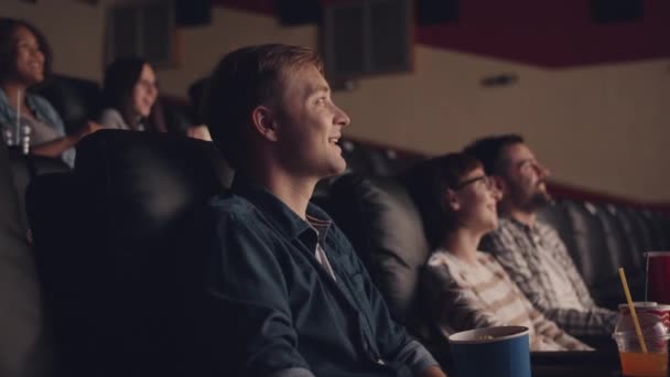 Vista lateral del joven viendo películas en el cine comiendo palomitas riendo — Vídeo de stock