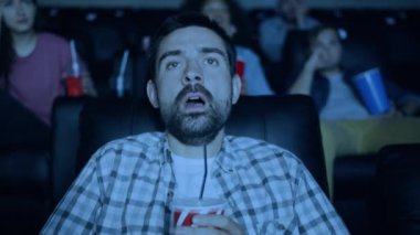 Korkmuş genç adam içki ile cam tutarak sinemada korku filmi izlerken