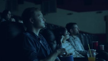Sinemada film izleyen gençlerin kalabalığı patlamış mısır yiyor gülümseyerek