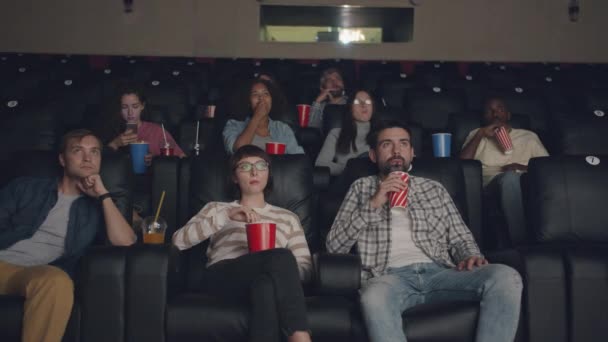 Movimiento lento del grupo multiétnico de estudiantes que ven películas en el cine comiendo — Vídeo de stock