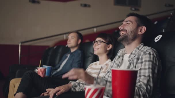 Медленное движение девушек и парней, смотрящих фильм в кинотеатре, смеющихся весело — стоковое видео