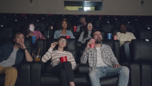 Расслабленная молодежь наслаждается кино в кинотеатре, ест попкорн и пьет веселье — стоковое видео