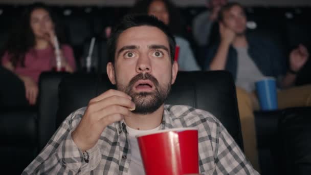Slow motion of scared guy eating popcorn watching shocking movie in cinema — Stock Video