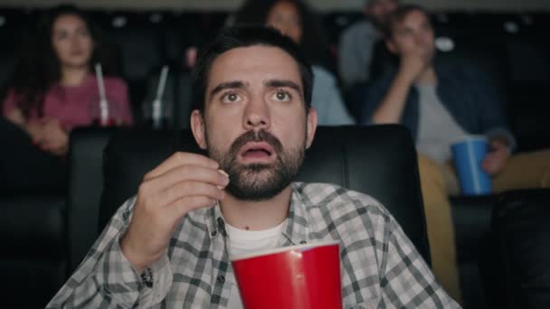 Shocked young man watching film in cinema with open mouth dropping popcorn — Stock Video