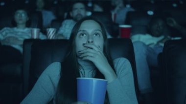 Sinemada patlamış mısır tutan açık ağızlı korku filmi izleyen korkmuş kadın