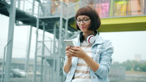 Щаслива молода леді торкається екрану смартфона, що стоїть на відкритому повітрі в самоті міста — стокове відео