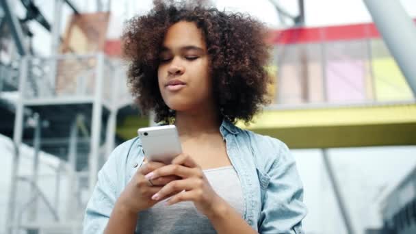 Afro-Amerikan bayan şehirde açık havada akıllı telefon ekranına bakarak gülüyor — Stok video