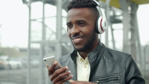 Afro-Américain dans les écouteurs chantant en utilisant smartphone en plein air — Video