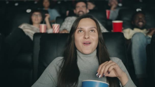 Slow motion of pretty brunette enjoying film in cinema laughing eating popcorn — Stock Video