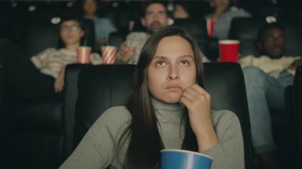 Frightened woman watching scary movie in cinema eating popcorn closing eyes — Stock Video