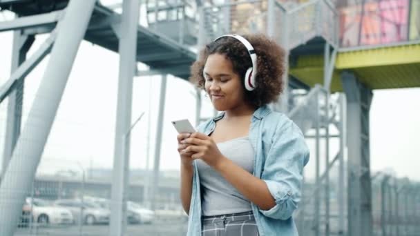 Медленное движение афроамериканского подростка, наслаждающегося музыкой, используя смартфон на открытом воздухе — стоковое видео