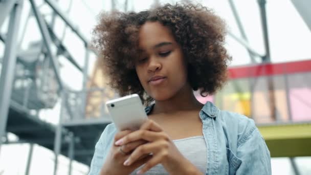 Afro-americano adolescente está usando smartphone moderno ao ar livre na rua — Vídeo de Stock