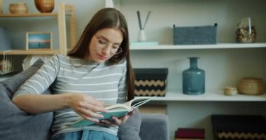 Gülümseyen genç kadın stüdyo dairede kapalı kitap okuma