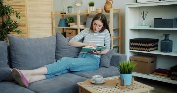 Приваблива молода жінка читає цікаву книгу, насолоджуючись літературою вдома — стокове відео