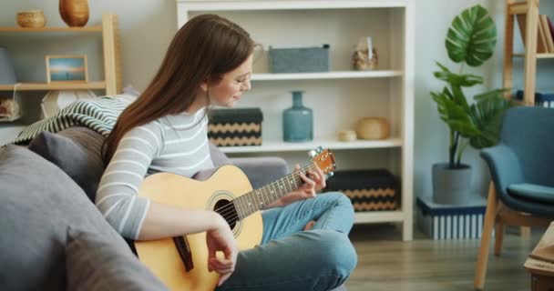 Câmera lenta de menina atraente gostando de música tocando guitarra no apartamento sozinho — Vídeo de Stock