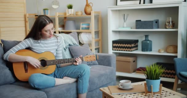 Όμορφη νεαρή γυναίκα που παίζει την κιθάρα σε φιλόξενο διαμέρισμα που διασκεδάζει μόνος — Αρχείο Βίντεο