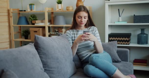 Красива молода жінка торкається екрану смартфона на дивані в будинку — стокове відео