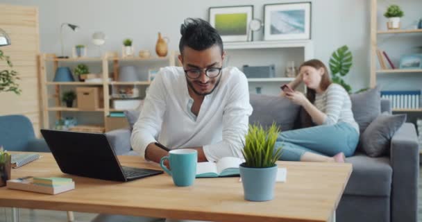 African American Guy werken thuis met laptop notebook, vrouw met behulp van smartphone — Stockvideo