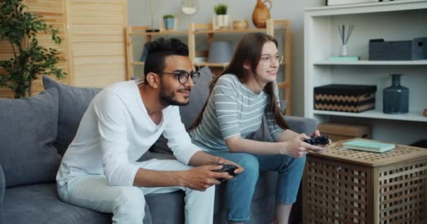 Girl and guy mixed race couple are enjoying video game at home using joysticks — Stock Video