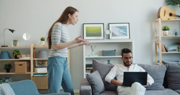 Człowiek za pomocą laptopa na kanapie w domu, podczas gdy zły kobieta krzyczeć na niego — Wideo stockowe