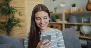 Akıllı telefon kullanan güzel kızın portresi sonra kameraya gülümseyerek bakıyor