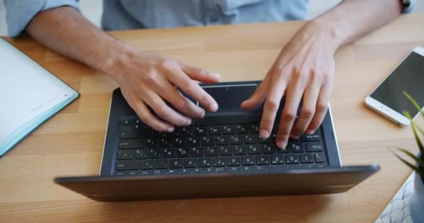 屋内のテーブルでラップトップのキーボードで入力する手のクローズアップ高角度ビュー — ストック動画