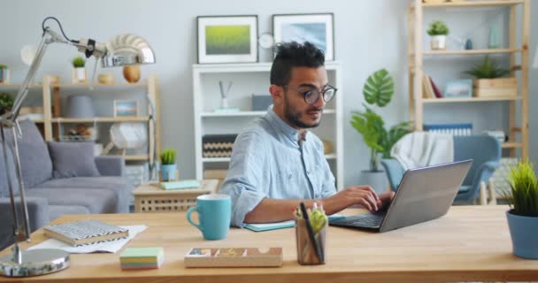 Красавчик-араб, работающий с ноутбуком и пишущий в блокноте дома — стоковое видео