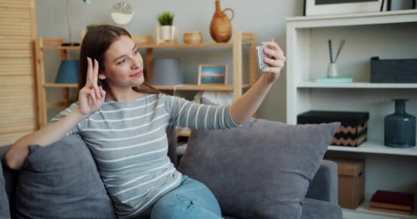 Ελκυστικό κορίτσι παίρνοντας selfie με κάμερα smartphone στον καναπέ στο σπίτι που ποζάρει — Αρχείο Βίντεο