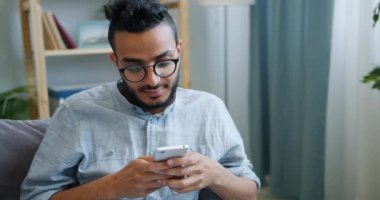 Mutlu genç Arap evde mutlu yüz ile ekrana bakarak akıllı telefon kullanarak