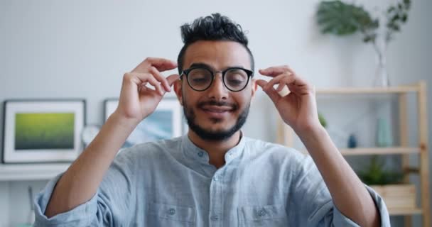 Retrato del hombre árabe quitándose las gafas mirando a la cámara sonriendo en casa — Vídeos de Stock