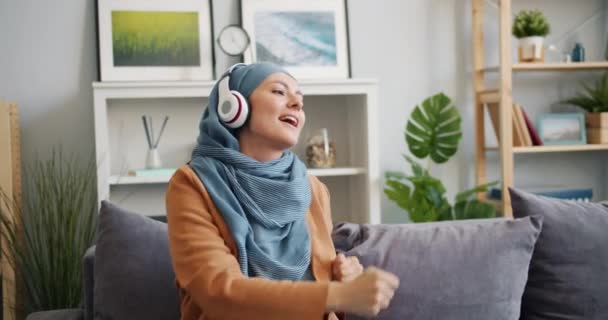 Moderna chica Mulsim en auriculares bailando disfrutando de la música en casa divirtiéndose — Vídeos de Stock