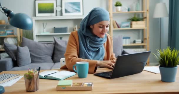 Chica independiente en hijab freelancer trabajando con portátil en apartamento — Vídeo de stock