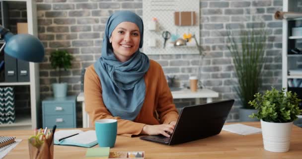 Portré a muszlim lány hidzsáb mosolyogva nézi kamera irodában az asztalon — Stock videók