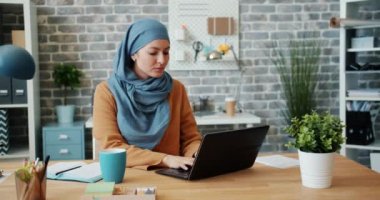 Dizüstü bilgisayar ile ofiste çalışan hijab çekici kadın sonra kamera bakarak