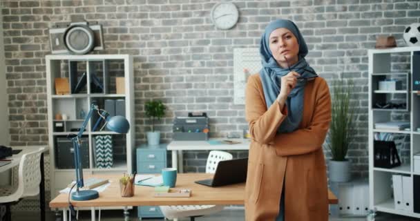 Γυναίκα μουσουλμάνος εργαζόμενος γραφείο σε χιτζάμπ στέκεται στο χώρο εργασίας κρατώντας γυαλιά — Αρχείο Βίντεο