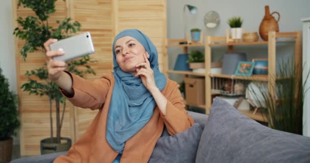 Menina muçulmana atraente no hijab levando selfie com câmera de smartphone em casa — Vídeo de Stock