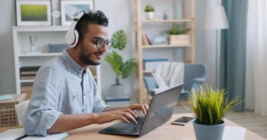 Afro-Amerikan adam dizüstü bilgisayar kullanarak ve evde kulaklık müzik dinleme