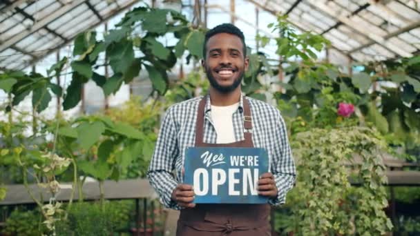 Afrikansk amerikansk man står i växthuset med vi är öppna skylt leende — Stockvideo