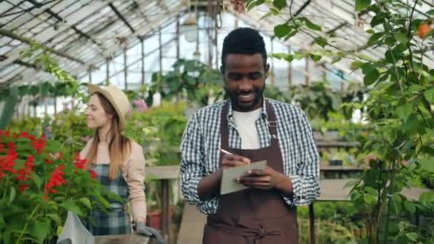 Business ägare gå i växthus skriver i anteckningsbok gör inventering leende — Stockvideo