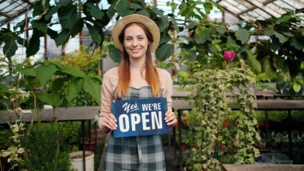 Mooie dame staande in kas met open teken glimlachend gastvrije kopers — Stockvideo