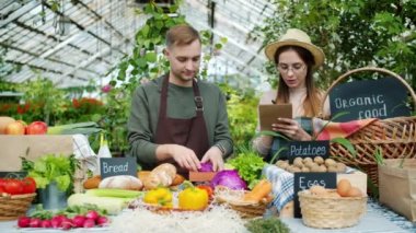Kız ve adam çiftçiler sera satışı masaya organik gıda koyarak konuşuyor