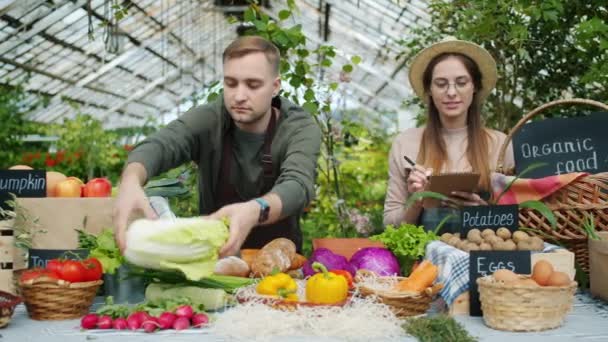 Jovens agricultores alegres colocando alimentos orgânicos na mesa nas vendas de fazendas — Vídeo de Stock