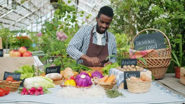 Αφρικανός Αμερικανός πωλητής βάζοντας φρέσκα βιολογικά λαχανικά στο τραπέζι σε πώληση αγροκτήματος — Αρχείο Βίντεο