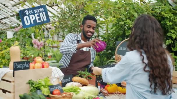 Vänlig afroamerikansk man som säljer bröd och kål till kund i marknaden — Stockvideo