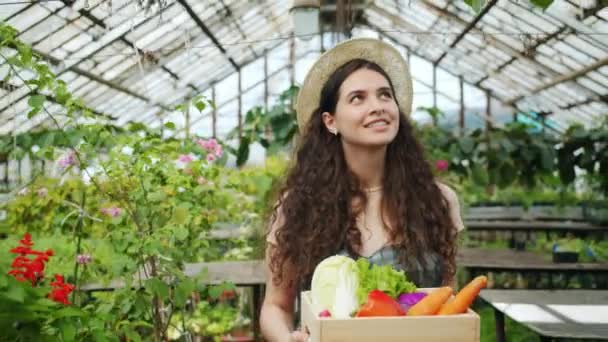 Портрет женщины-фермера, гуляющей в теплице с коробкой органических овощей — стоковое видео