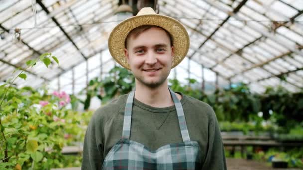 Portrait of handsome man farmer wearing hat and apron standing in greenhouse — Stockvideo
