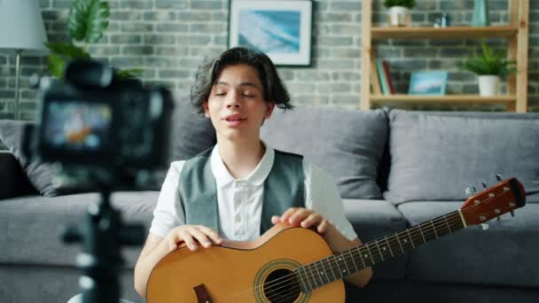 Мальчик-подросток записывает видео для онлайн-видеоблога с жестом в руках гитары — стоковое видео